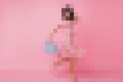 Person wearing a pink outfit stands against a pink background, holding a small blue bag.