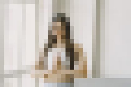 A person standing indoors near a light sofa in a neutral-toned room.