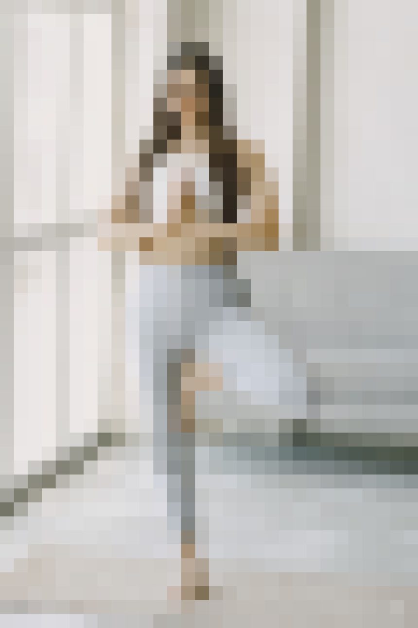 A person standing indoors near a light sofa in a neutral-toned room.