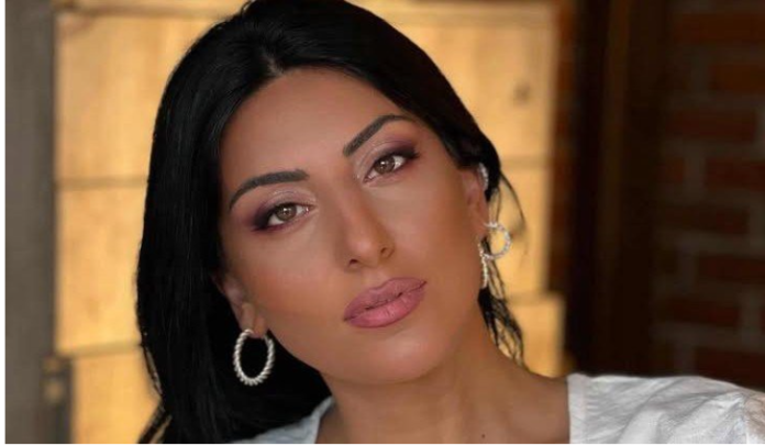 Portrait of a woman with dark hair, light makeup, pink lips, wearing hoop earrings, looking at the camera in a warm setting