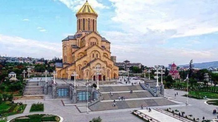 Golden-domed cathedral on a stepped plaza overlooking a town, with wide stairs and lampposts in the foreground.